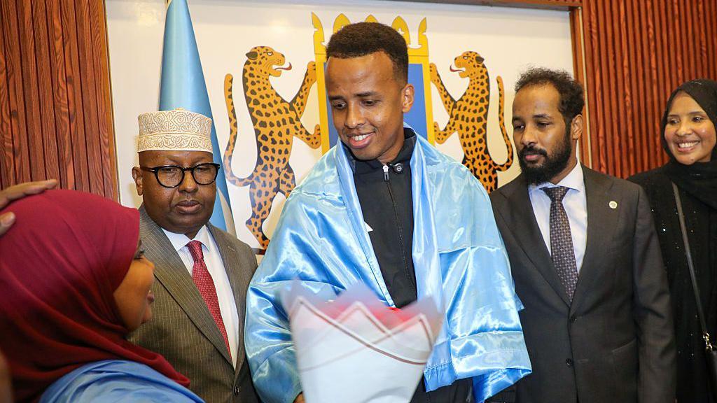 Omar Ardan, el árbitro somalí, sonriendo y sosteniendo la bandera de Somalia